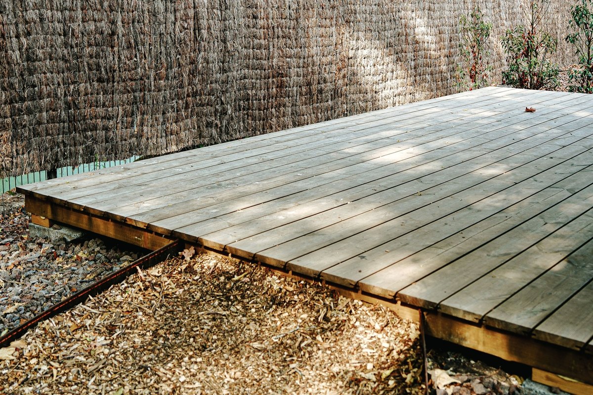 New low wooden deck platform of plank boards on a visible frame beside a reed fence