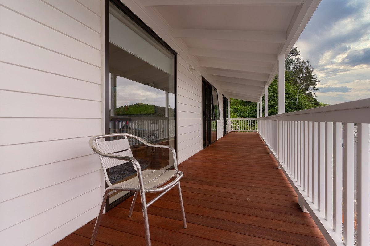 Covered porch deck with reddish-brown deck boards and a white railing on a white horizontal-board house