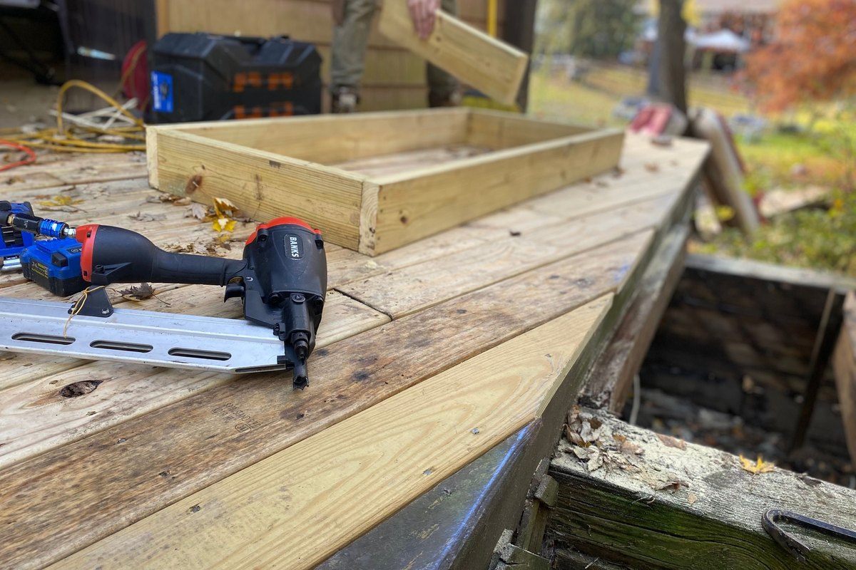 Nail gun and a new pressure-treated board on a deck being rebuilt beside rotted old framing
