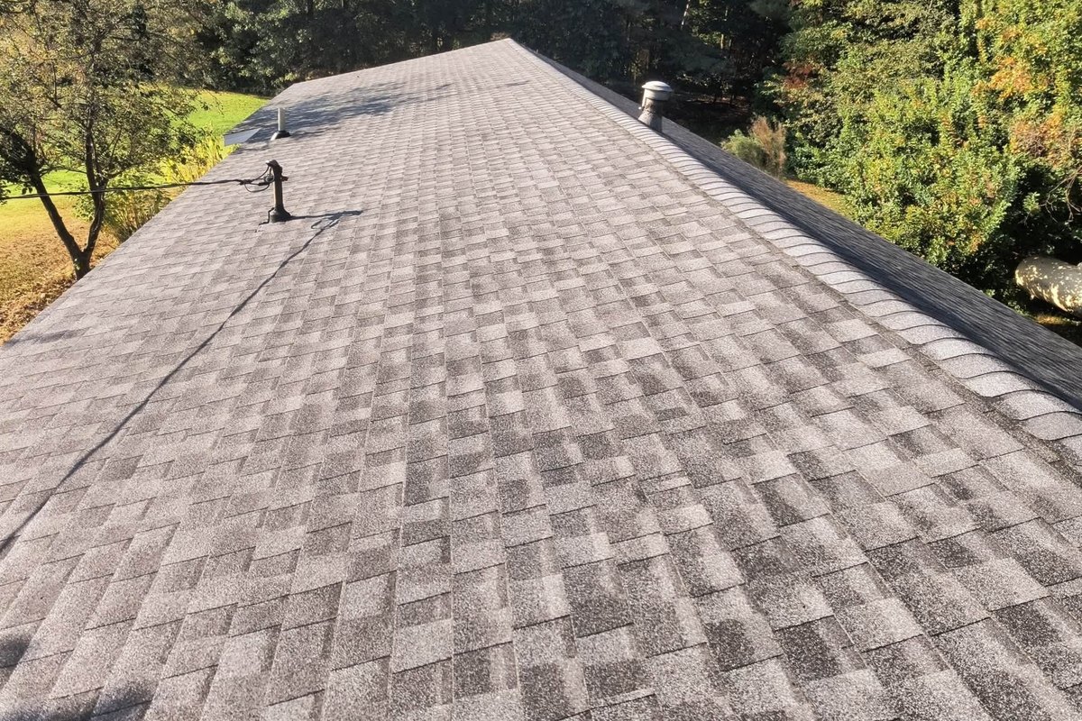 Finished gray-brown asphalt shingle roof seen from above with a capped ridge and roof vents