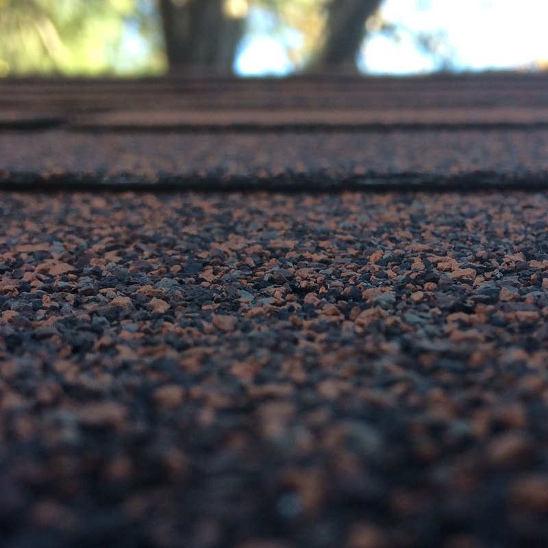 Close-up of dark asphalt roof shingle granules with a blurred sky behind