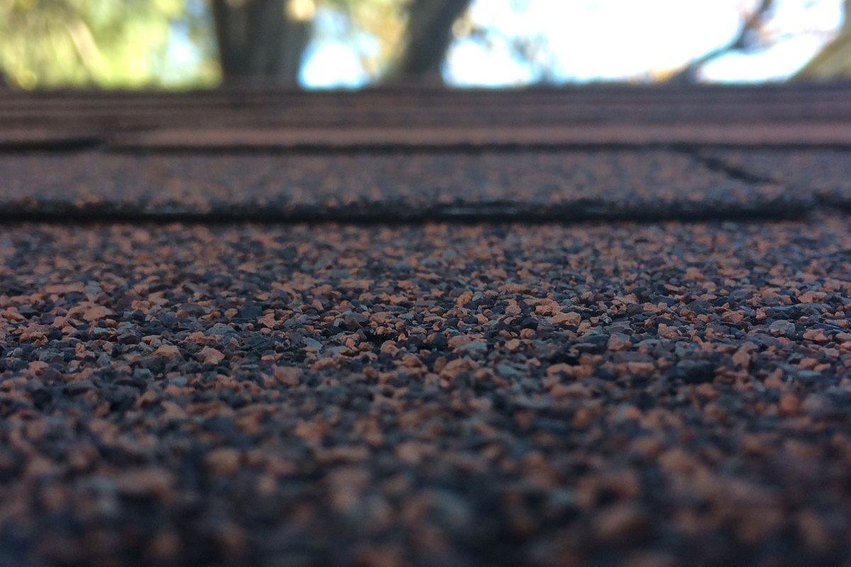 Close-up of dark asphalt roof shingle granules with a blurred sky behind