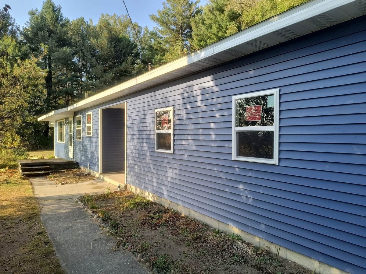 One-story ranch house in periwinkle blue vinyl siding with two new windows and a recessed entry