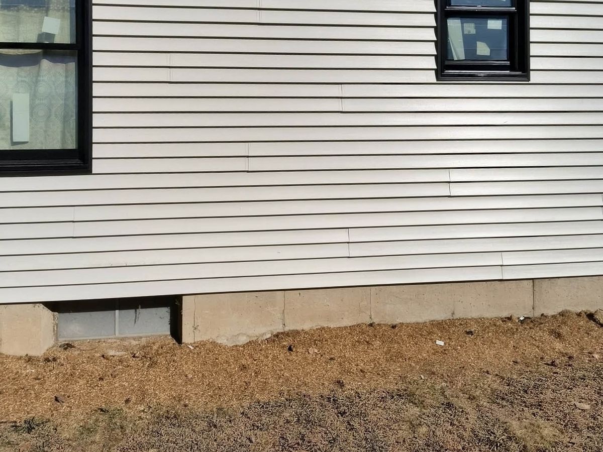 Gable end of a house in beige vinyl siding with two new black-framed windows and black soffit