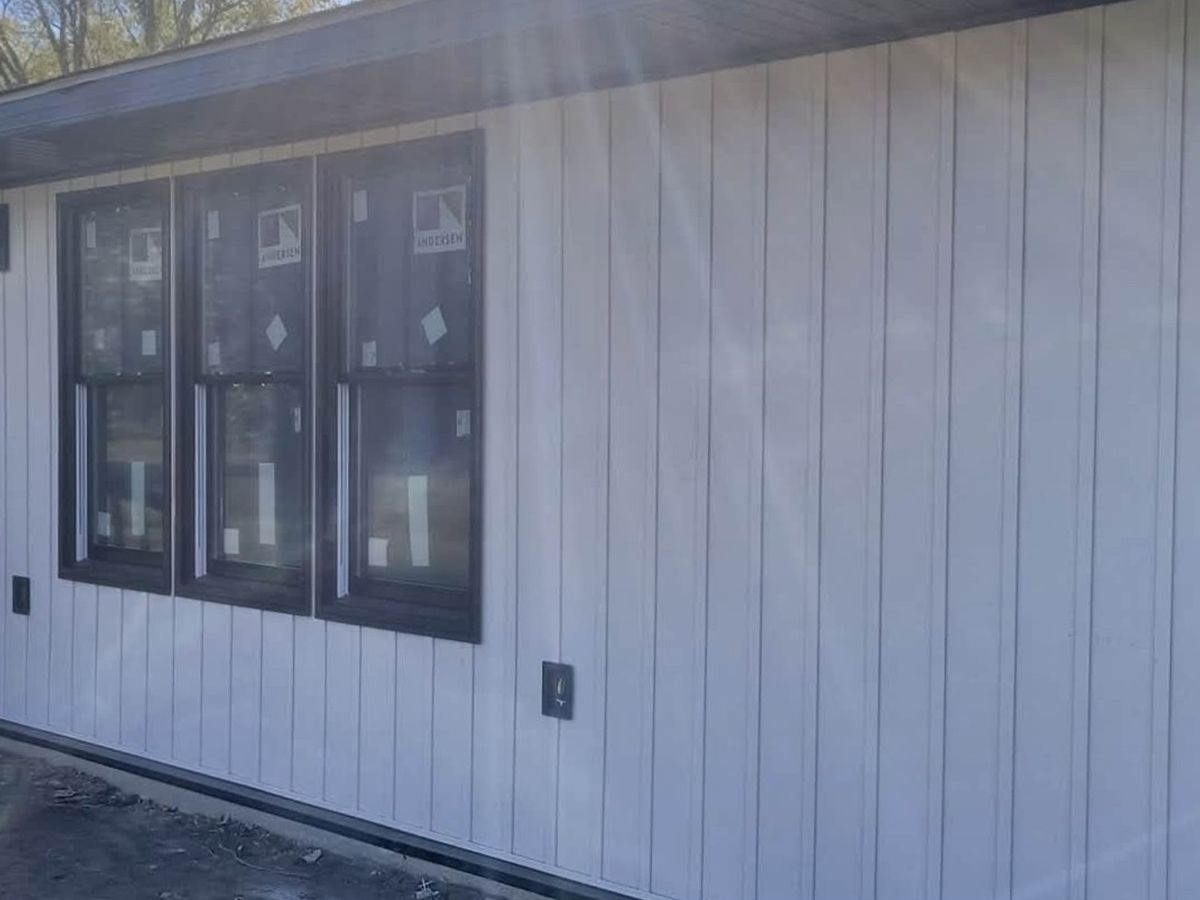 White vertical vinyl siding on a one-story house with three new black-framed windows