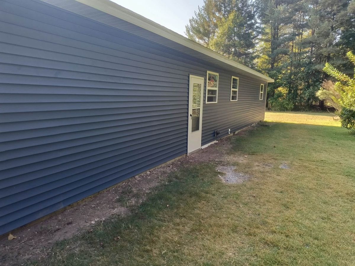 Long side wall of a one-story house in dark slate blue vinyl siding with a white entry door and small windows
