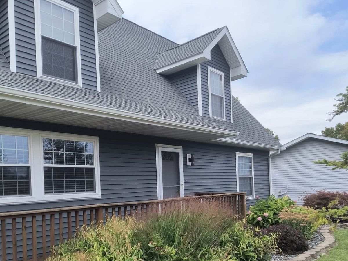 Two-story cape-style house in slate gray vinyl siding with dormers, bay windows and a wood porch deck