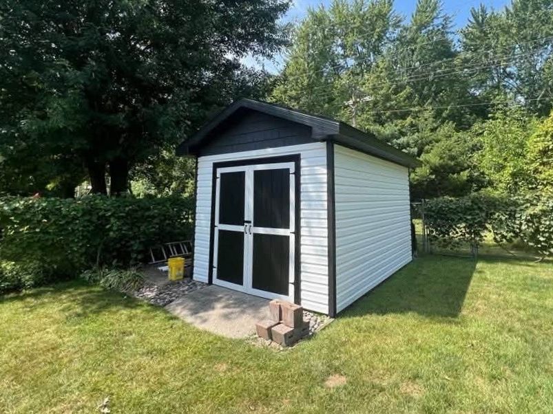 Backyard shed with white horizontal vinyl siding, black trim and black double doors