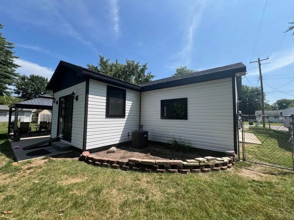 White horizontal vinyl siding on a small house with black trim, a glass door and a gazebo at the left