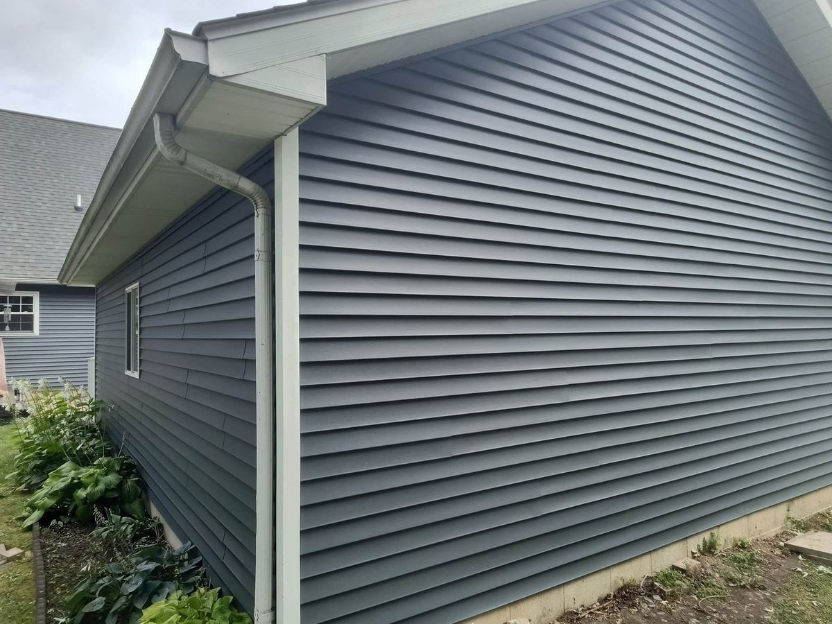 Slate blue-gray horizontal vinyl siding on a house wall with white soffit, gutter and downspout