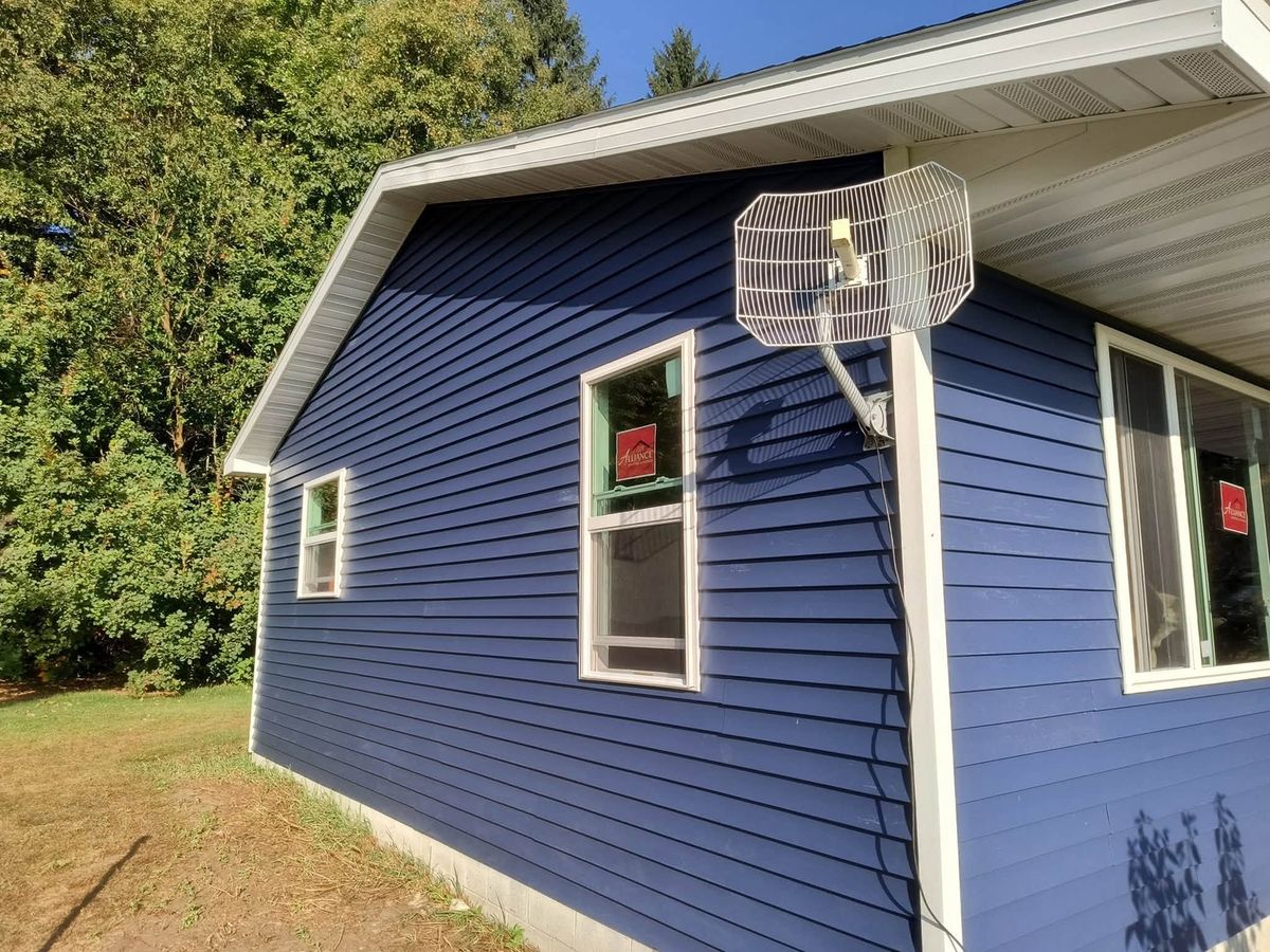 Navy blue vinyl siding on a house corner with two new windows still carrying red stickers