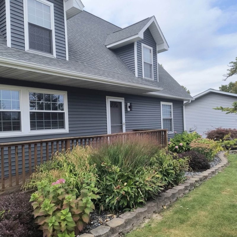 Two-story cape-style house in slate gray vinyl siding with dormers, bay windows and a wood porch deck