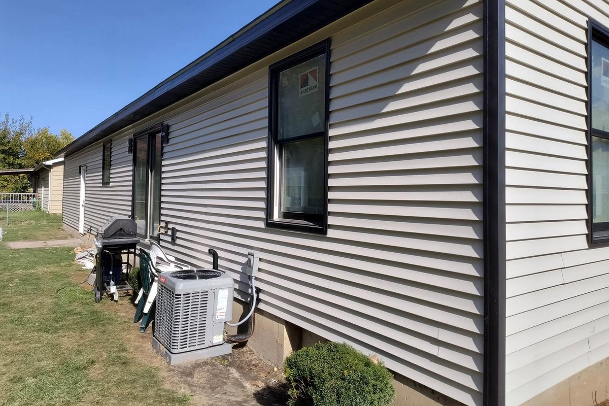 Beige vinyl-sided ranch wall with black-framed new windows and a sliding door