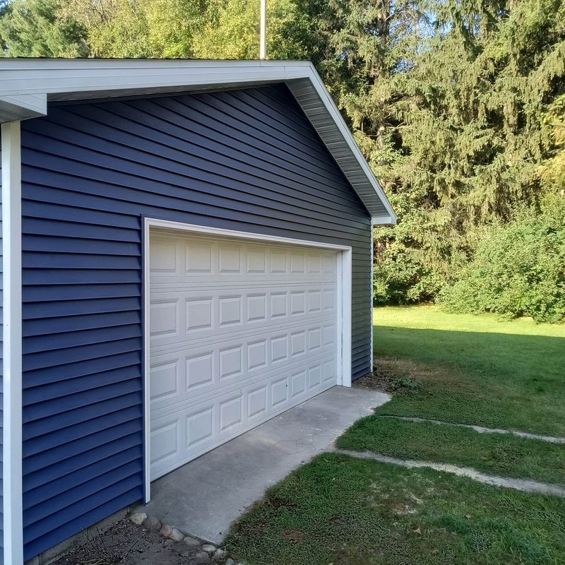 Detached garage with navy blue horizontal vinyl siding, white trim and a white overhead door