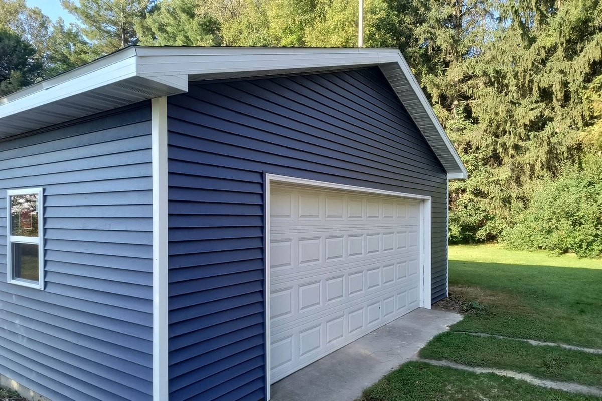 Detached garage with navy blue horizontal vinyl siding, white trim and a white overhead door