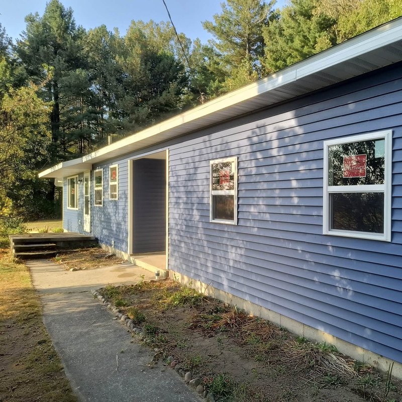 One-story ranch house in periwinkle blue vinyl siding with two new windows and a recessed entry