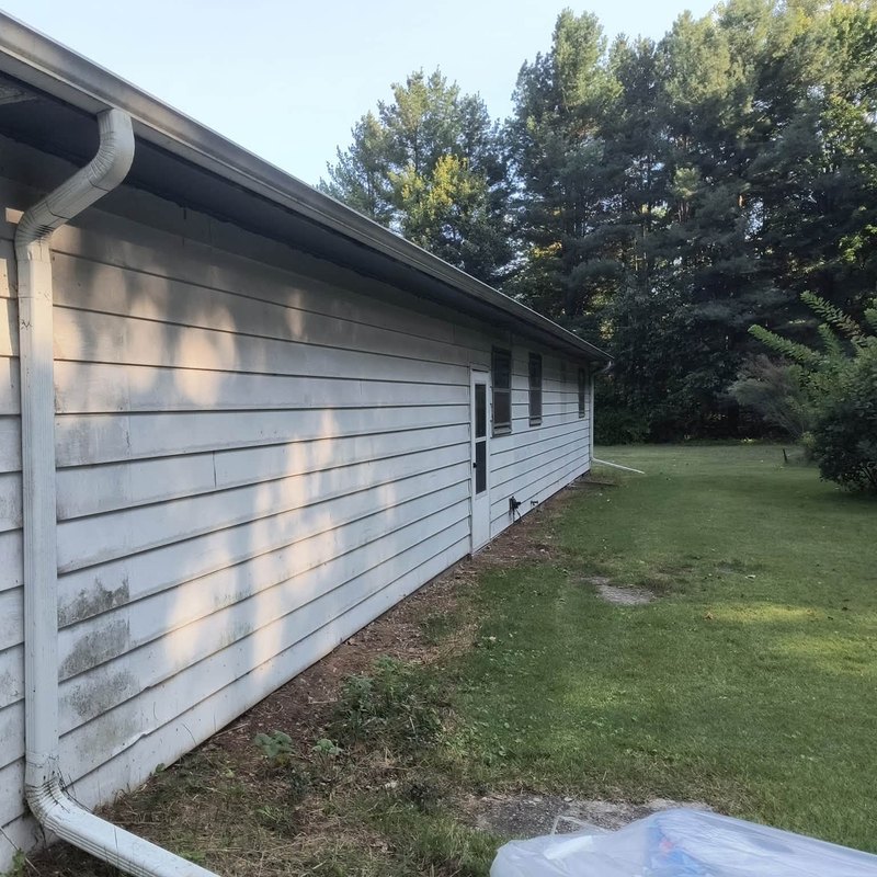 Old white lap siding stained with gray-green mildew along a low building with an attached garage door