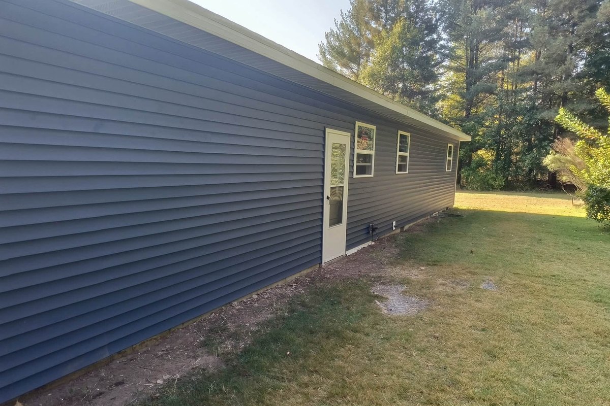Long side wall of a one-story house in dark slate blue vinyl siding with a white entry door and small windows