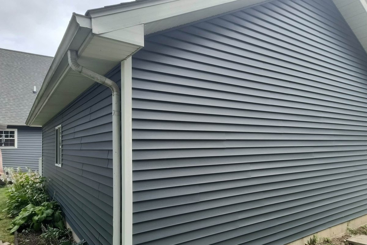 Slate blue-gray horizontal vinyl siding on a house wall with white soffit, gutter and downspout