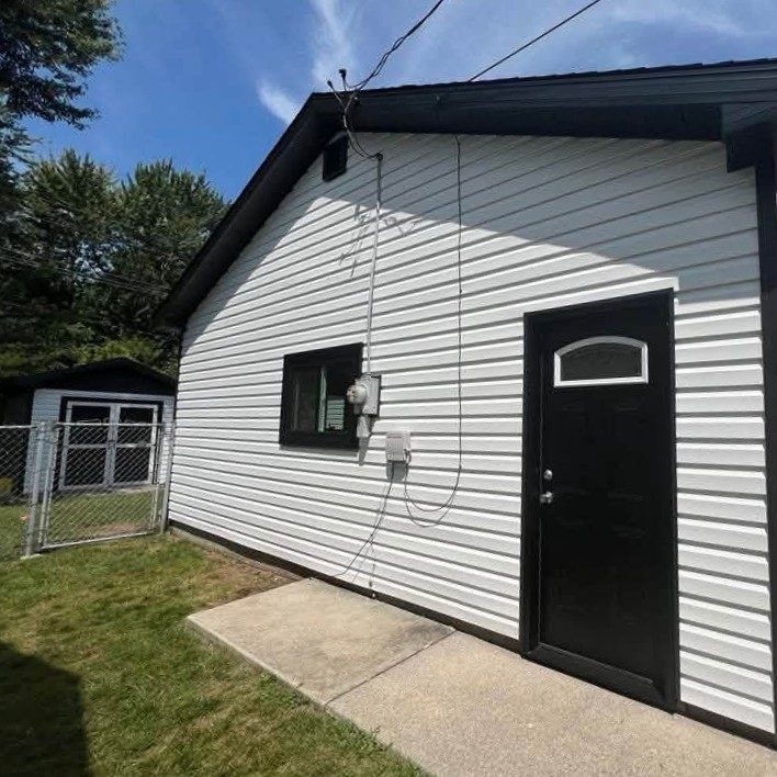 Small house corner in white horizontal vinyl siding with black trim and a black entry door