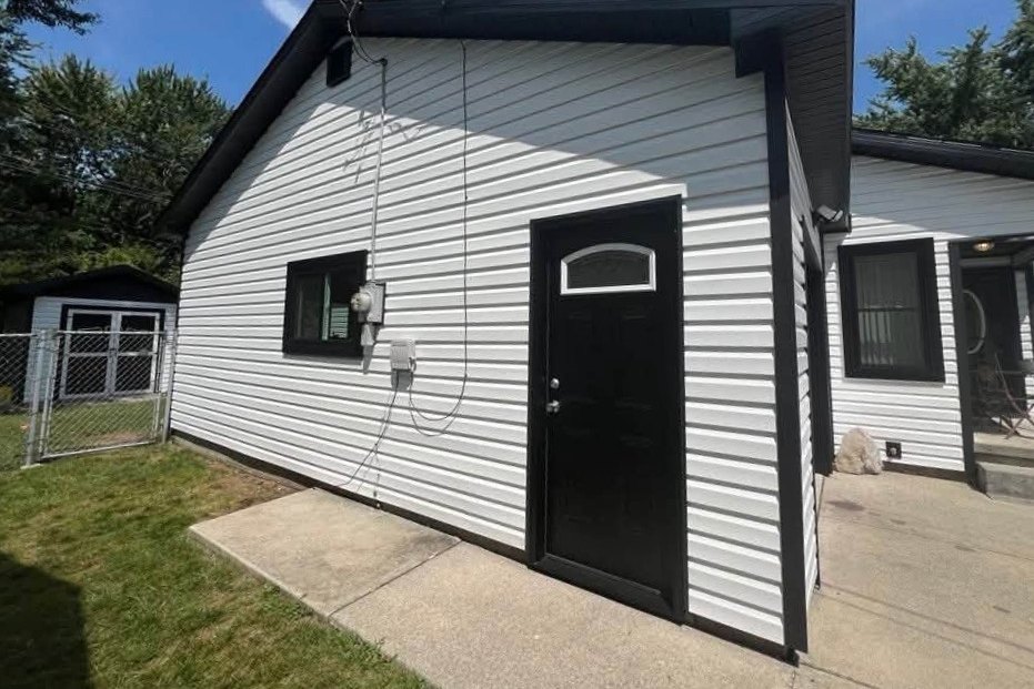 Small house corner in white horizontal vinyl siding with black trim and a black entry door