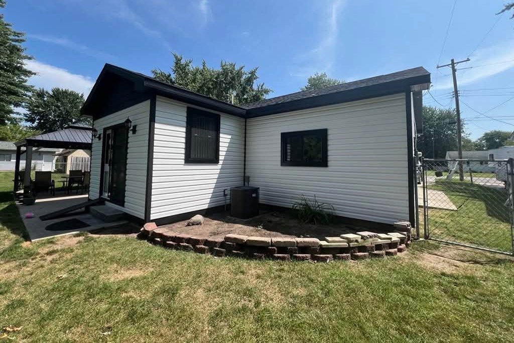 White horizontal vinyl siding on a small house with black trim, a glass door and a gazebo at the left