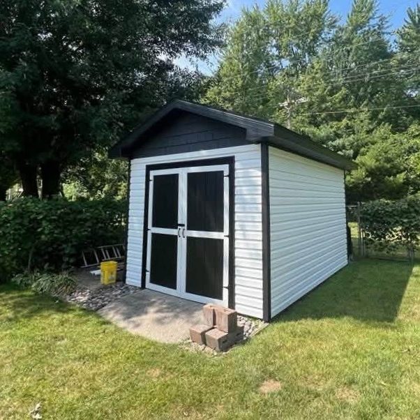 Backyard shed with white horizontal vinyl siding, black trim and black double doors