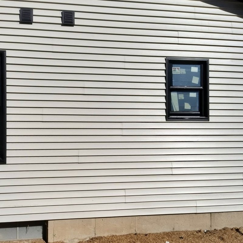 Beige horizontal vinyl siding on a house wall with black-framed new windows