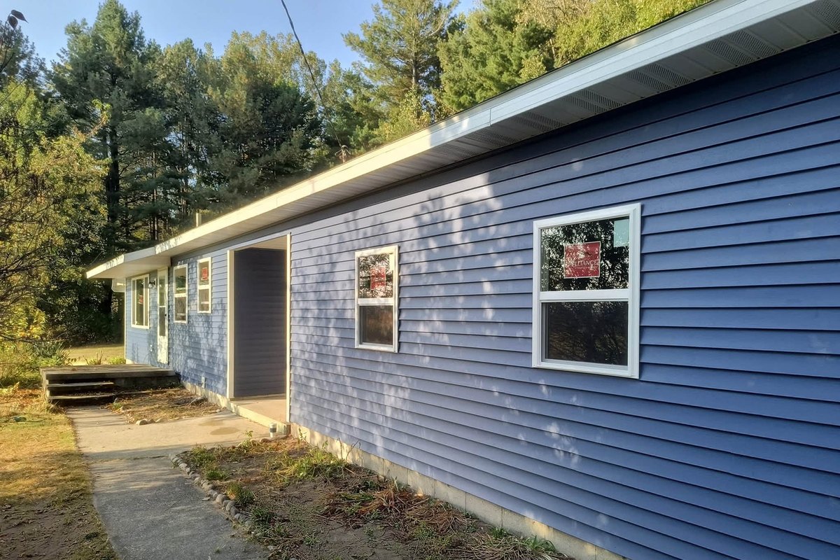 One-story ranch house in periwinkle blue vinyl siding with two new windows and a recessed entry