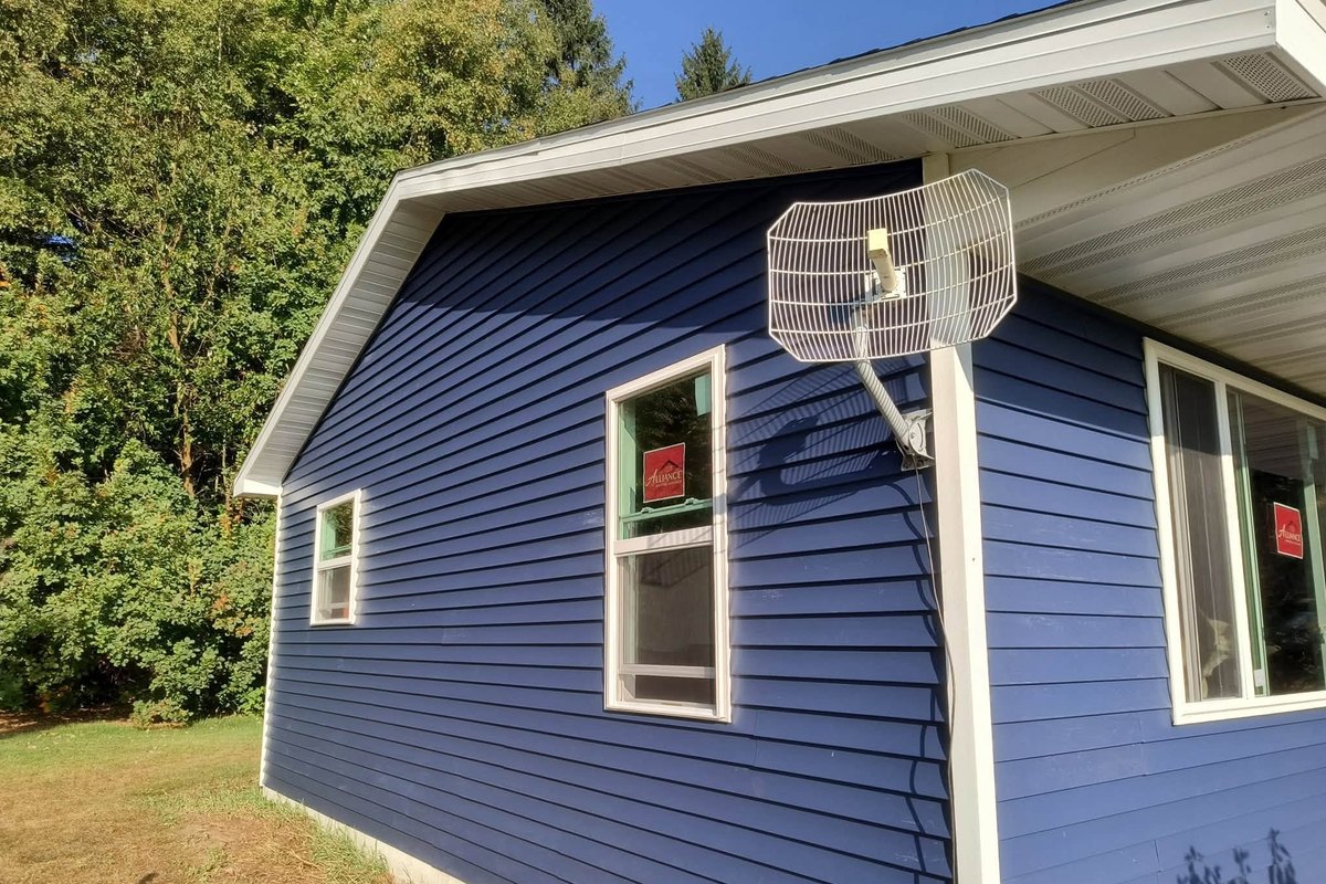 Navy blue vinyl siding on a house corner with two new windows still carrying red stickers
